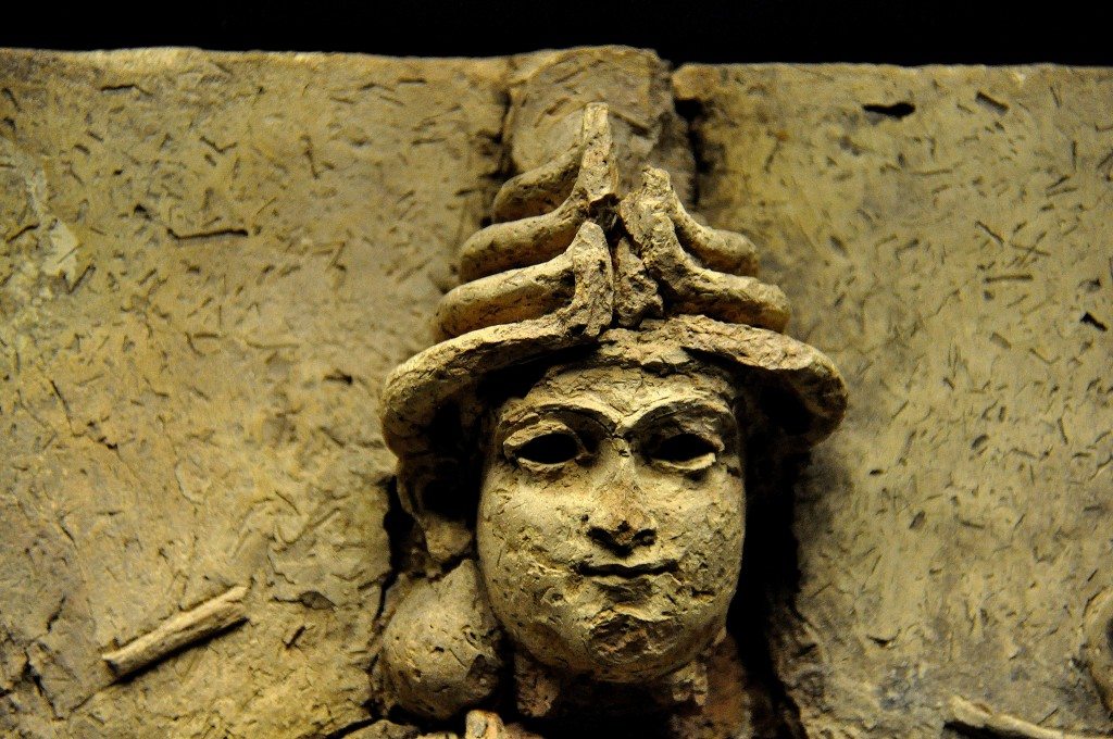 A close-up image of the face of the female deity. Note the hollow eyes, full cheeks, and joined eyebrows. The upper left horn of her headdress and the left hair bun are lost. 