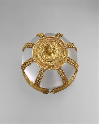 ​Hairnet with Medallion, ca. 200–150 BCE. The luxurious nature of this gold hairnet, or kekryphalos, which would have been owned by a woman of high status, attests to the wealth of the Greek Hellenistic world. A substantial amount of hair would have been required to secure this complex and expensive accessory at the back of the head. It can be compared to the hairnet worn by Arethusa on the Syracusan coin (no. 18). Containment defines the purpose of this gold object, and yet its central medallion shows a maenad (follower of Dionysos, god of wine), who personifies abandon. Even her hair seems to escape the confines of a grape vine wreath. Hairnets of this type have been associated with Ptolemaic Egypt, where the ruling families included queens such as Berenike II (no. 32) and Cleopatra VII, who was famous for her love affairs with Julius Caesar and Mark Antony.