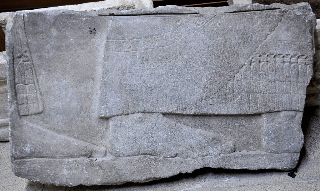 This fragment was labeled, at the left upper part, using Arabic language, "م م ق 380" which means Mosul Museum 380. Note the "horizontal slit" at the upper margin, which seems to be caused by electric saw, during the cutting process of the relief. The relief shows part of the lower legs of 2 men, bare-footed. They wear long firnged robe, exquisitely carved. It is unknown whether this fragment came from the North-West Palace or from another palace within Nimrud, or from other Assyrian palaces in Nineveh or Dur-Sharrukin. Not on display. Exclusive photo; never-before-published. The Sulaymaniyah Museum, Iraqi Kurdistan. Photo © Osama S. M. Amin. 