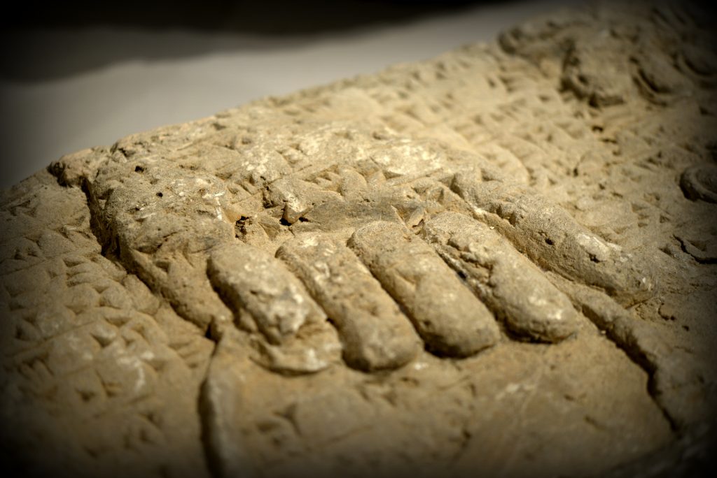 Detail of a gypsum wall relief from the North-West at Nimrud. What has survived is a left hand of an Apkallu (Akkadian, which means sage). The hand grips on the handle of a buckle. The buckle is supposed to contain a fluid (?water for purification). The cuneiform text of the so-called "Standard Inscription" of Ashurnasirpal II runs over the relief. At the right upper angle, part of the "Sacred Tree" appears. Photo © Osama S. M. Amin. 